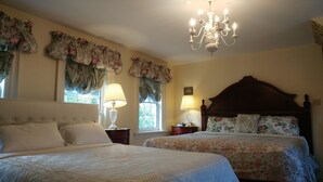 A bedroom with two beds, floral curtains, a chandelier, and a wooden headboard.