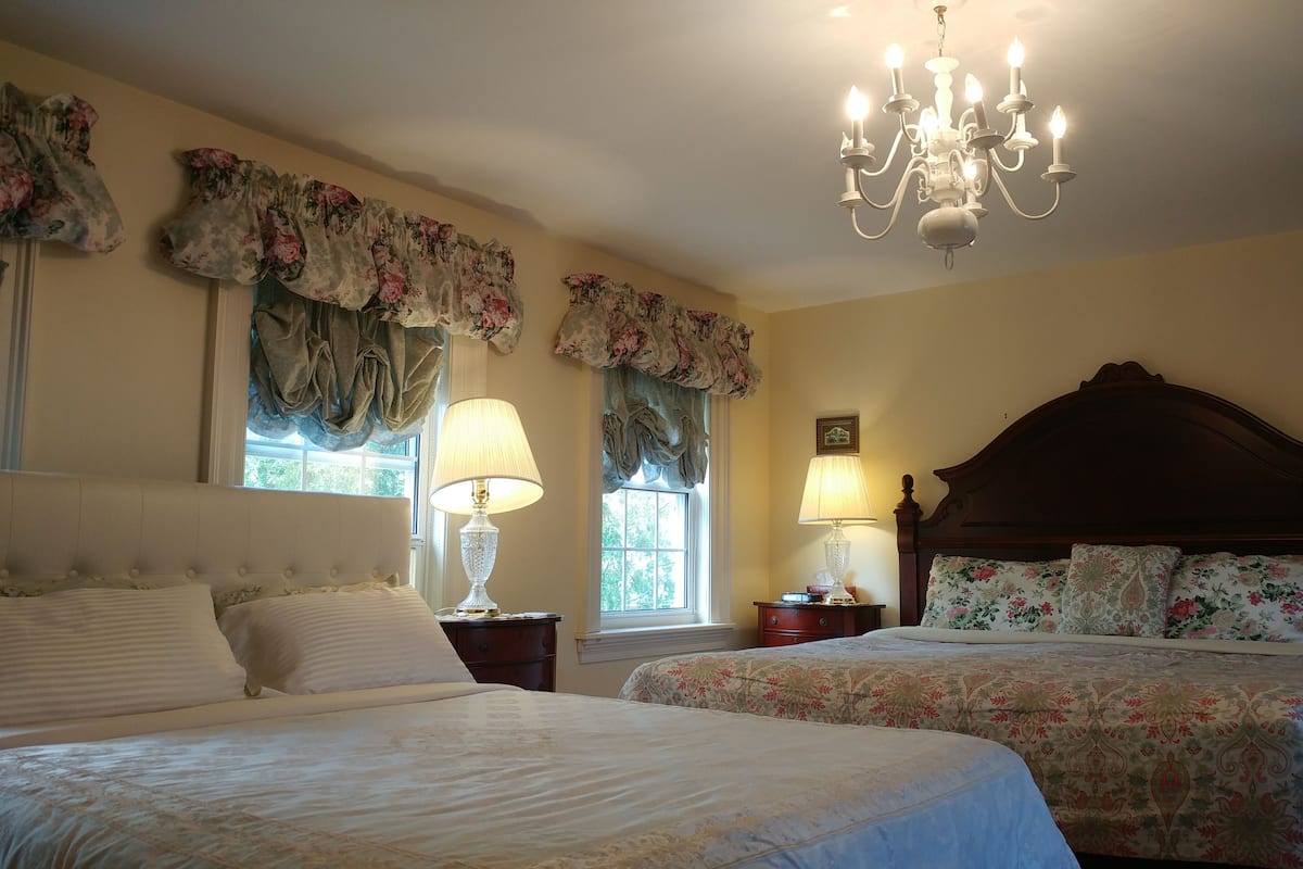 A bedroom with two beds, floral curtains, a chandelier, and a wooden headboard.