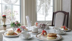 A breakfast table set with tea, coffee, and pastries, with a view of flowers outside.