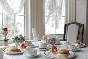A breakfast table set with tea, coffee, and pastries, with a view of flowers outside.