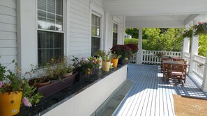 A covered porch with a wooden deck, potted plants, and a dining area with wooden furniture. - Inn on Frederick (St. Andrews)