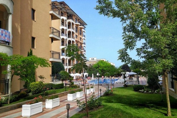 A hotel courtyard with a swimming pool, outdoor seating, and lush greenery.