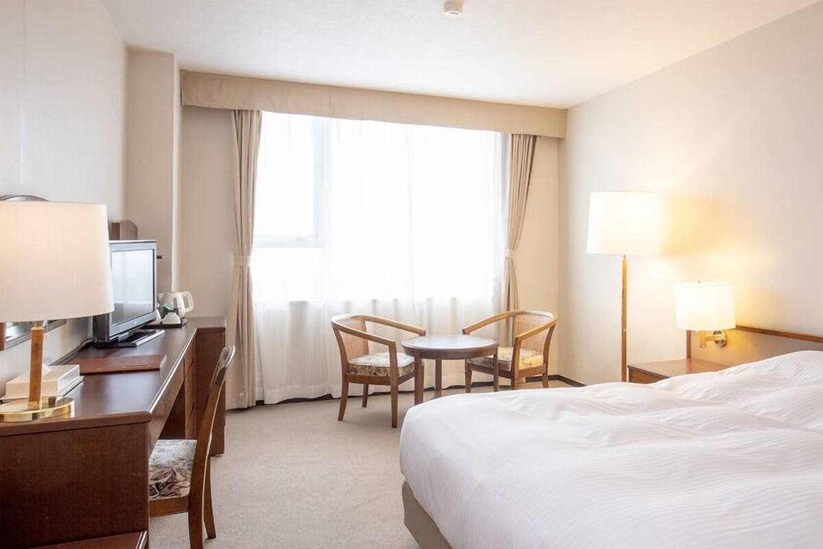 A hotel room with a bed, desk, chair, TV, and lamps.