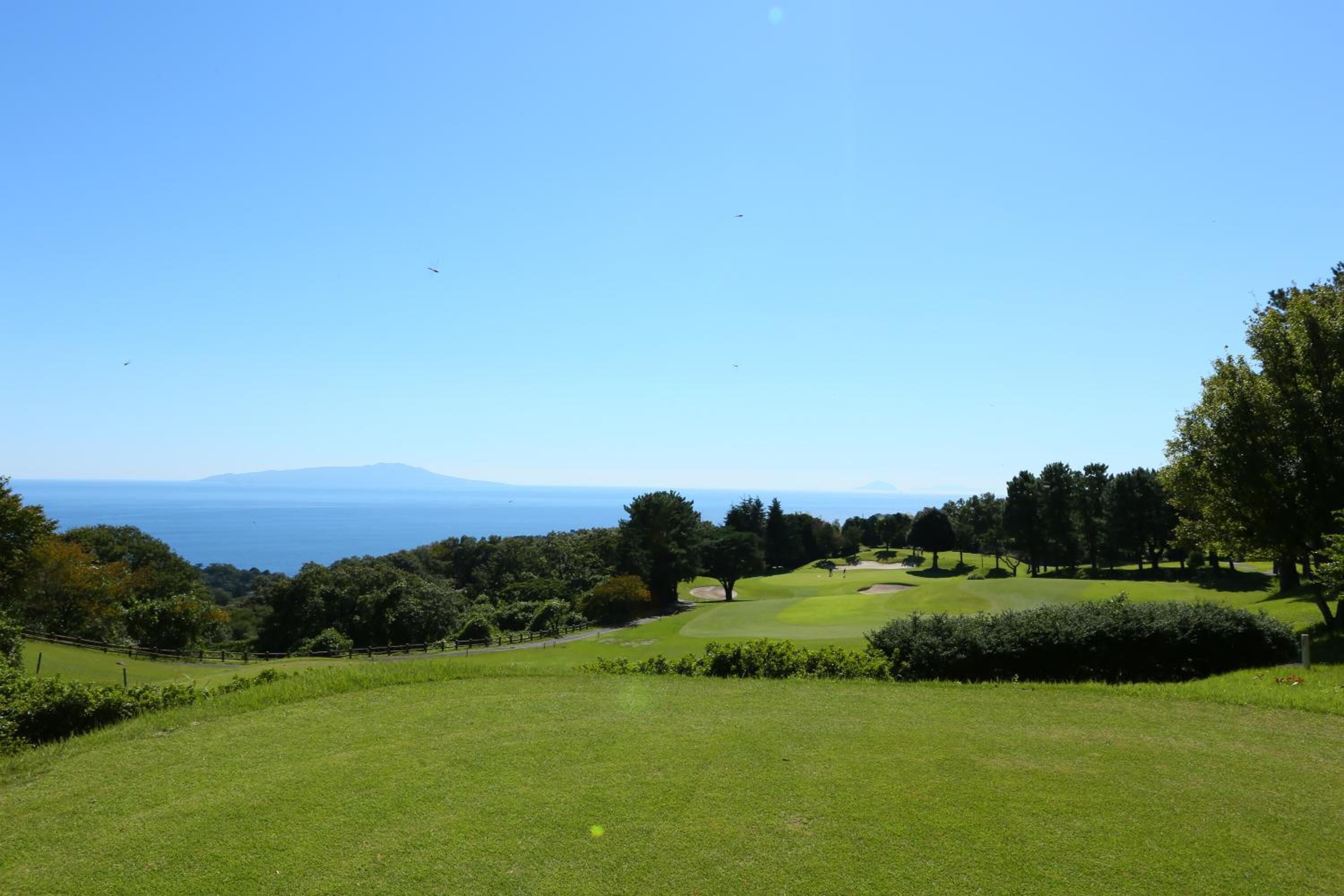 A golf course with a clear view of the ocean and distant mountains.