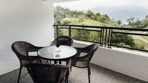 A balcony with wicker furniture and a glass table, overlooking a mountainous landscape. - Sun Moon Lake Residence 8 (Yuchi)
