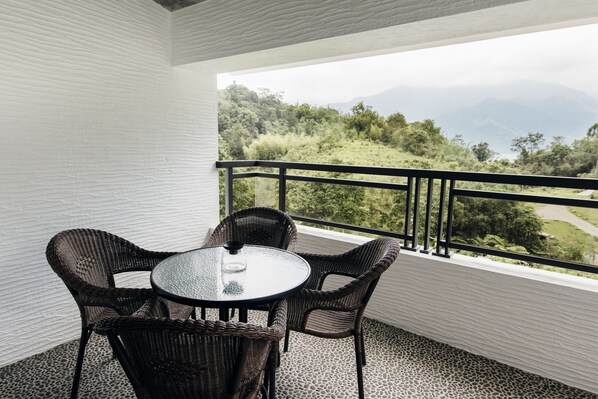 A balcony with wicker furniture and a glass table, overlooking a mountainous landscape. - Sun Moon Lake Residence 8 (Yuchi)