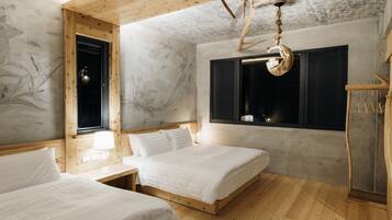 A room with two beds, wooden flooring, a window with curtains, a hanging light fixture, and a wall with a tree mural.