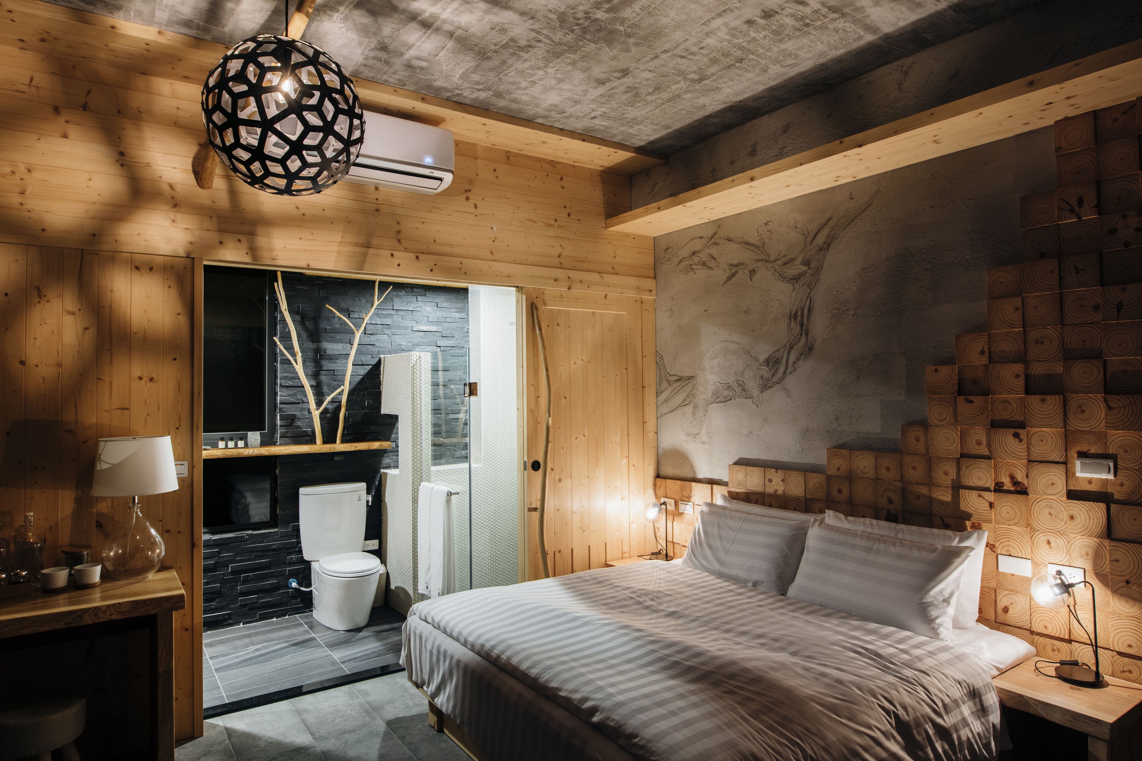 A modern bedroom with a wooden ceiling, a bed with white bedding, a nightstand with a lamp, and a wall-mounted heater.