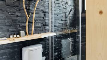 Un baño moderno con pared de piedra, techo de madera, inodoro y cabina de ducha de vidrio.