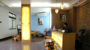 A hotel reception area with a wooden reception desk, a receptionist, and a large window. - Fubin Hostel (Hengchun)