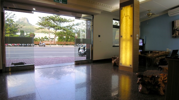 A hotel lobby with a glass door leading outside, a reception desk, and a wooden column. - Fubin Hostel (Hengchun)