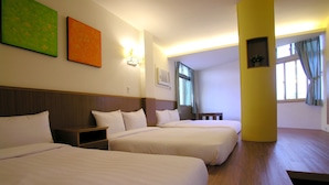A hotel room with two beds, a wooden headboard, a nightstand, a wall-mounted lamp, and a window with curtains. - Fubin Hostel (Hengchun)