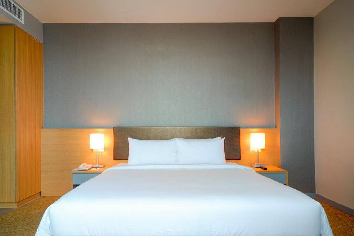 Ein Hotelzimmer mit einem großen Bett, zwei Nachttischen mit Lampen und einem Holzschrank.