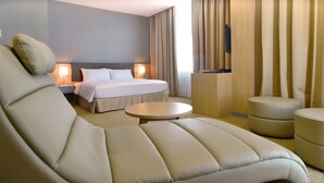 A hotel room with a large bed, two bedside tables with lamps, a sofa, a small round table, and a TV mounted on the wall. - Hotel N°5 (Kota Kinabalu)