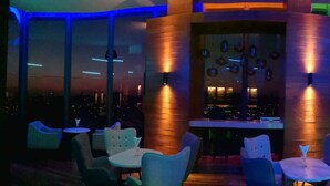 A modern bar area with a long counter, multiple seating options, and a view of the city at night. - Hotel N°5 (Kota Kinabalu)