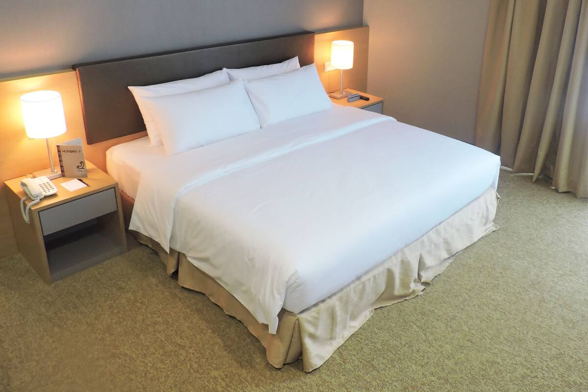 Ein ordentlich bezogenes Bett mit weißen Laken, zwei Nachttischlampen, ein Nachttisch mit Telefon und eine Wandlampe.