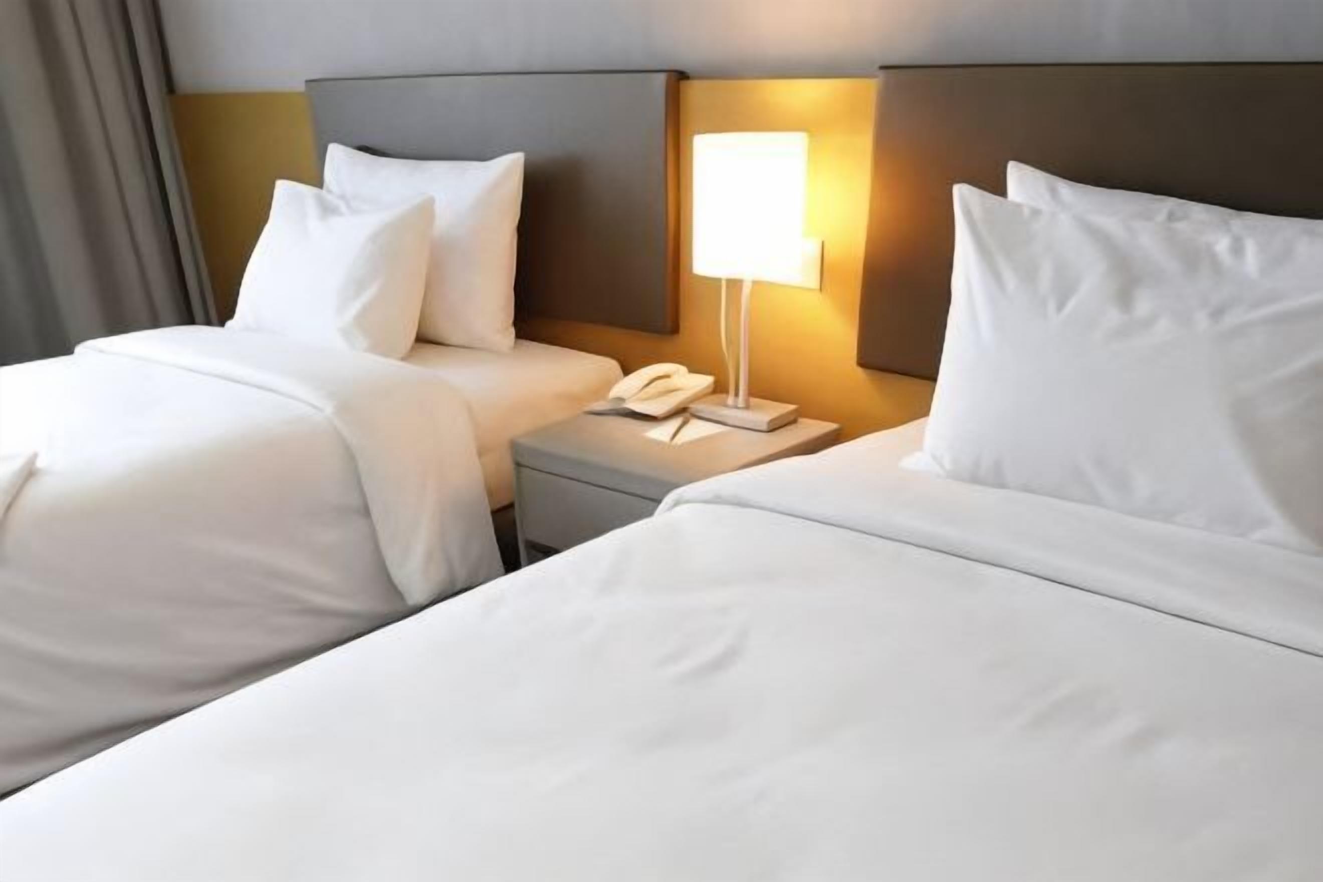 A hotel room with two beds, a bedside table with a lamp, and a telephone.