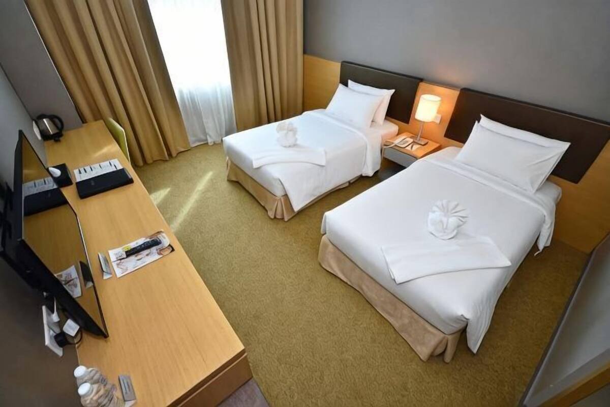 Ein Hotelzimmer mit zwei Betten, einem Schreibtisch, einem Computer, einem Fernseher und einer Lampe.