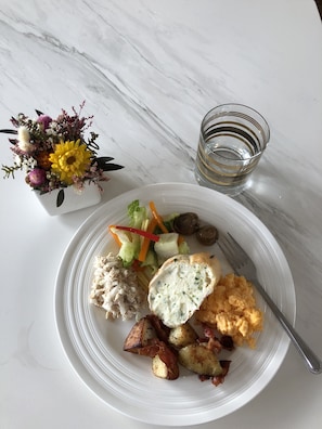 A white plate with a salad, potatoes, and a creamy dish, a glass of water, and a small vase with flowers on a marble table. - Hotel Everyday Life (Hengchun)