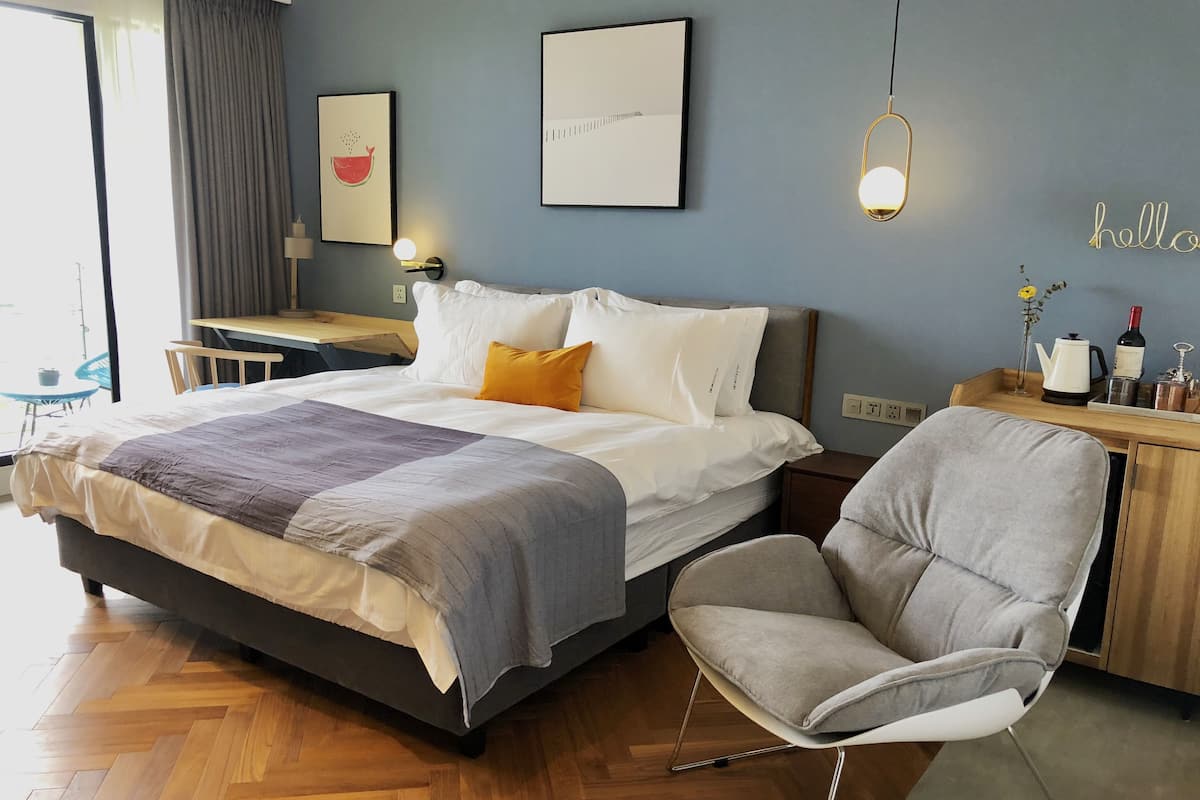 A modern hotel room with a bed, a desk, a chair, and a view of the outdoors.
