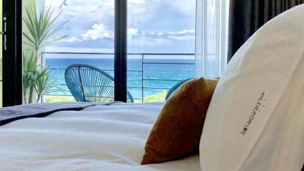 A hotel room with a bed, a view of the ocean, a chair, and a window with curtains. - Hotel Everyday Life (Hengchun)