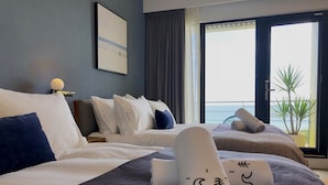A hotel room with a large bed, a smaller bed, a window with a view of the sea, and a potted plant. - Hotel Everyday Life (Hengchun)