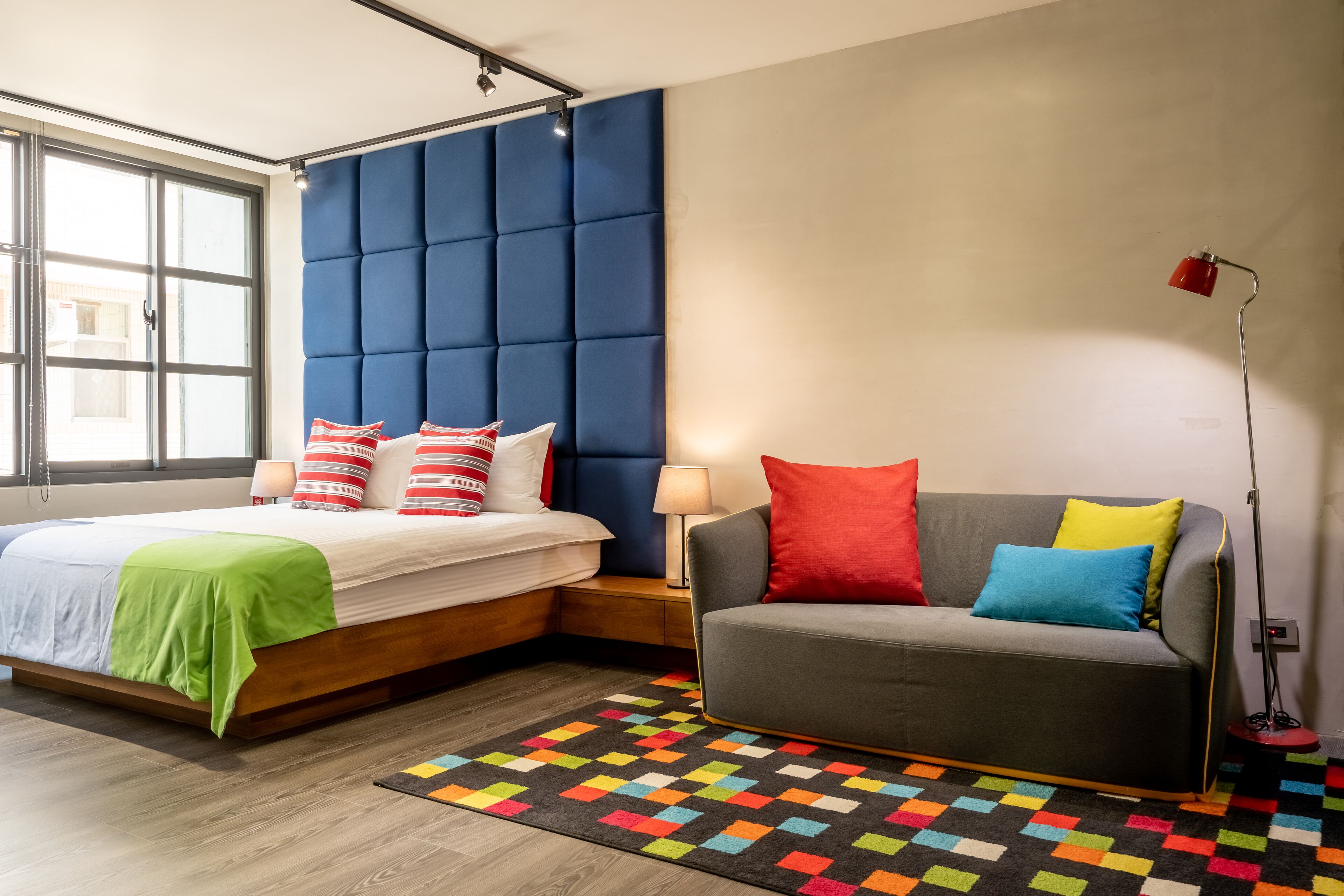 Une chambre moderne avec un lit, un canapé, un tapis coloré et une fenêtre.