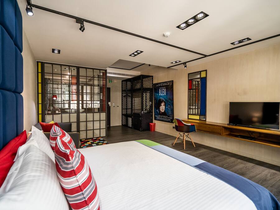 Una habitación de hotel moderna con una cama grande, un televisor y una zona de estar con una silla y una mesita.
