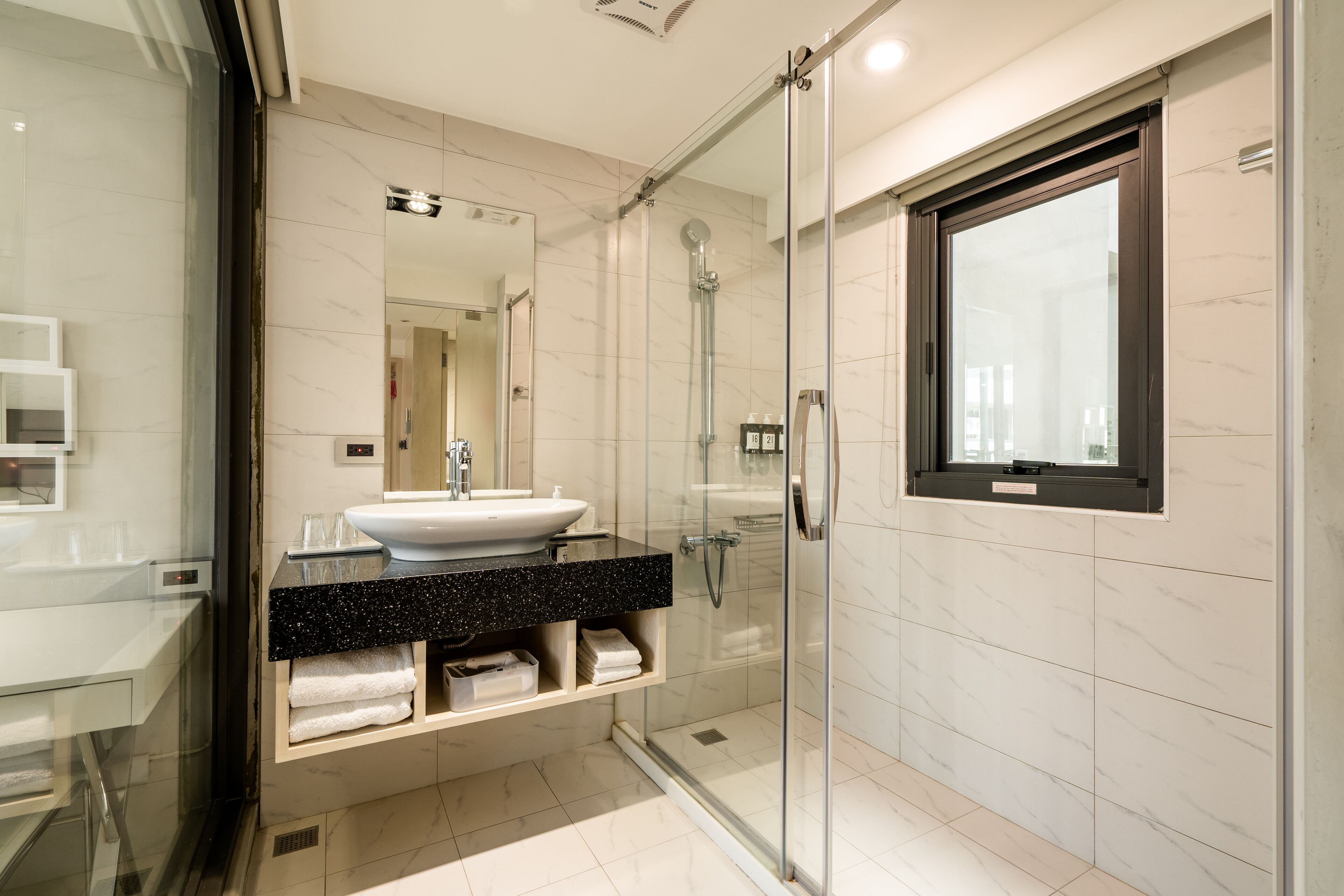 A modern bathroom with a glass-enclosed shower, a white sink, and a marble-tiled floor.