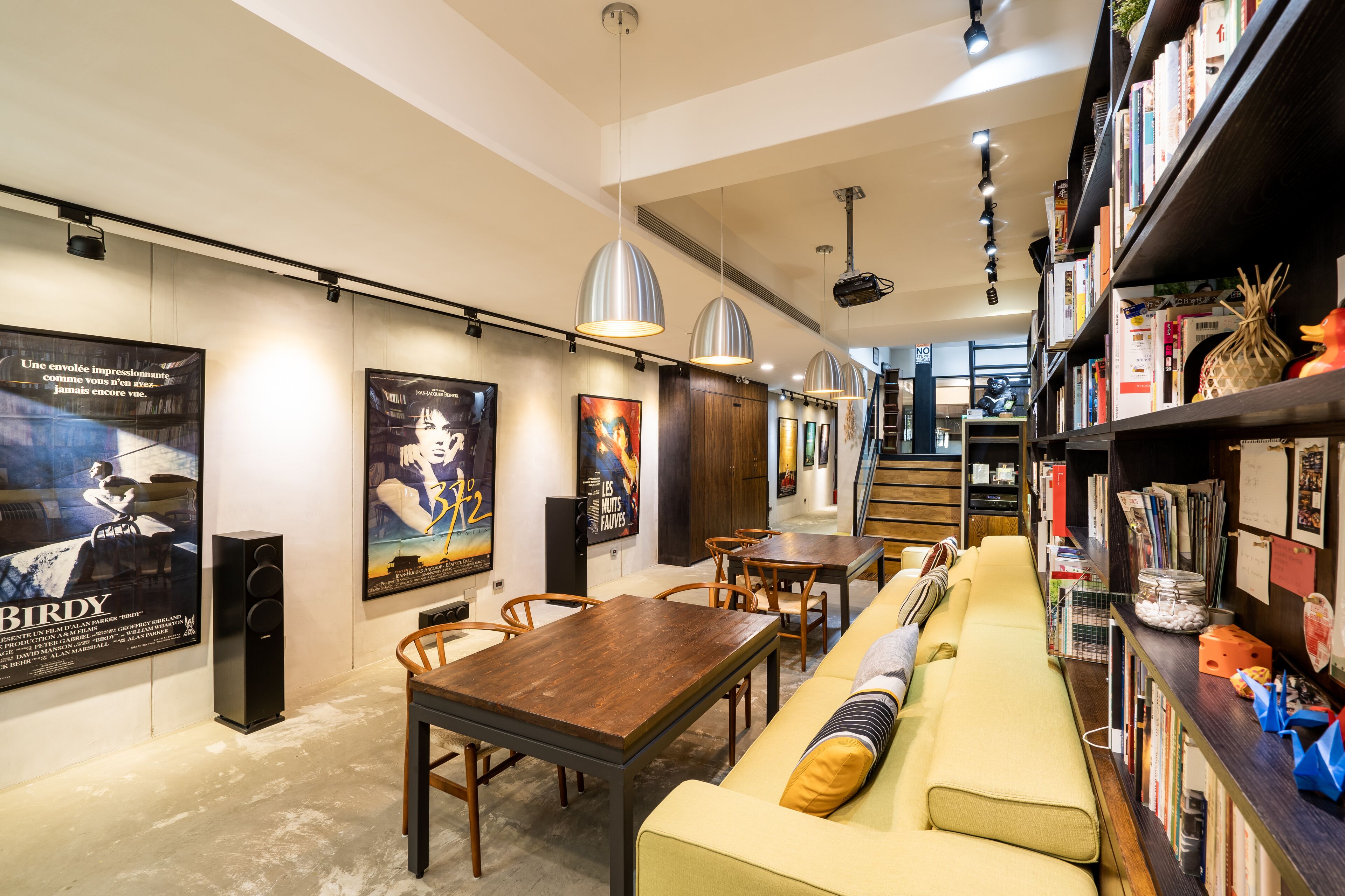 A modern interior with a wooden dining table, a yellow sofa, and a bookshelf filled with books and decorative items.