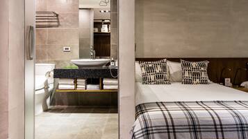 A modern bathroom with a sink, toilet, and towel rack. The room features a bed with plaid bedding and patterned pillows.