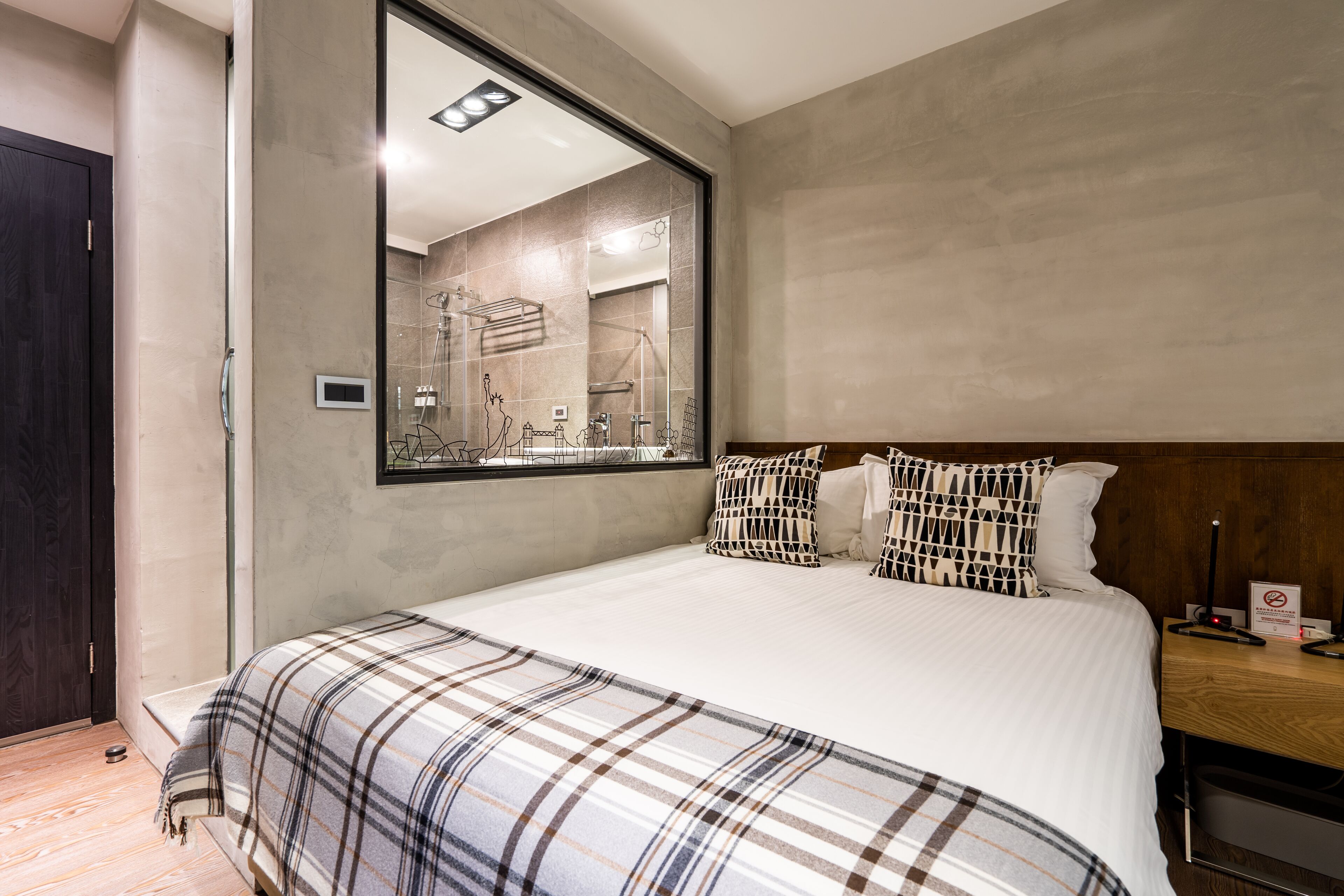 Une chambre d’hôtel moderne avec un grand lit, une tête de lit en bois, un grand miroir et un plancher en bois.