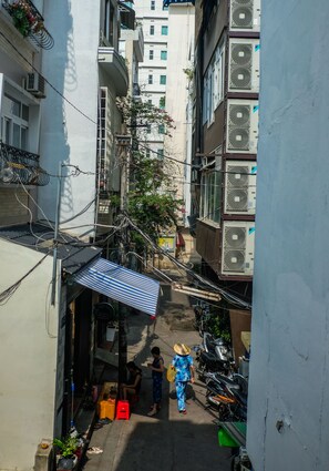 A narrow alleyway between buildings with air conditioning units, a small shop, and a person walking. - The PM Hostel (Da Lat)