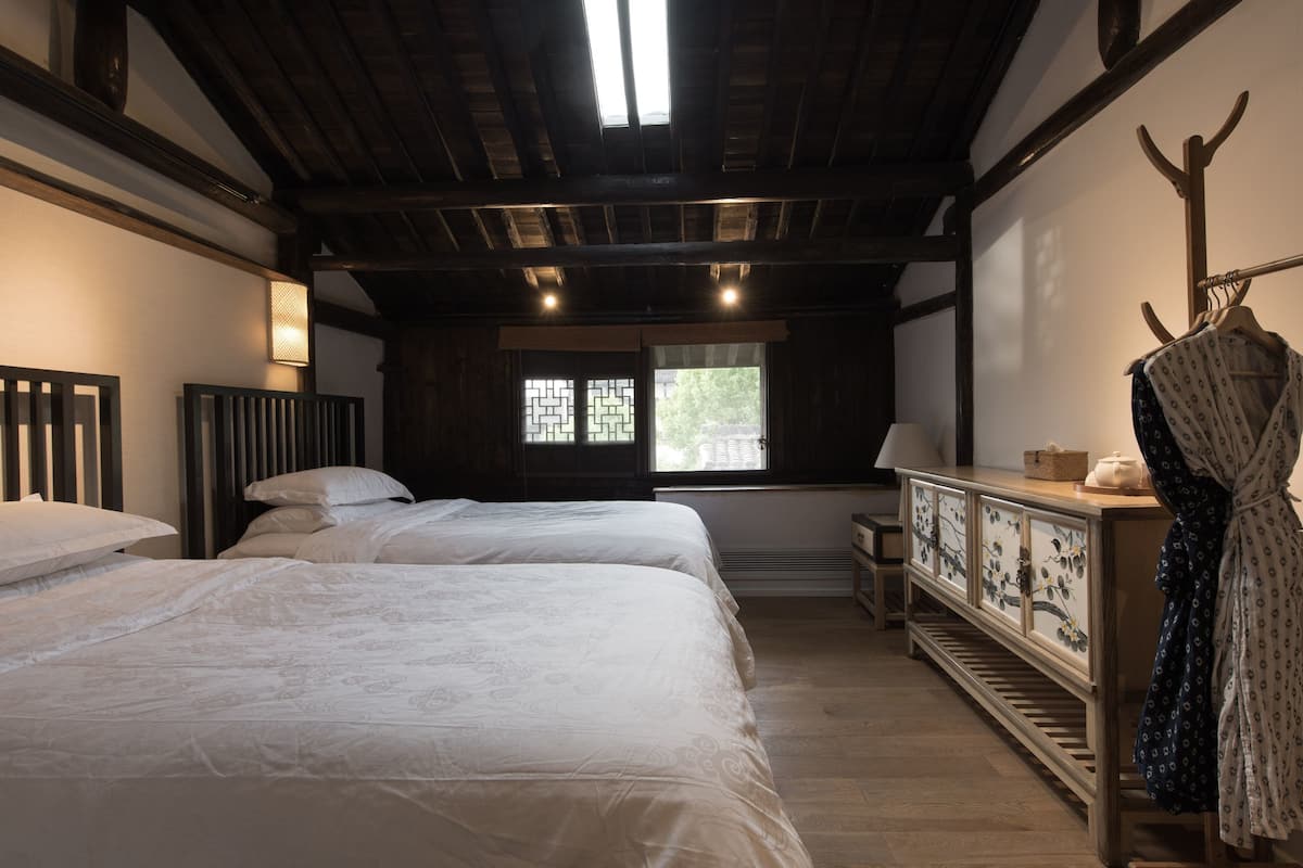 Un dormitorio con dos camas, un aparador de madera, un perchero y una ventana con vistas.