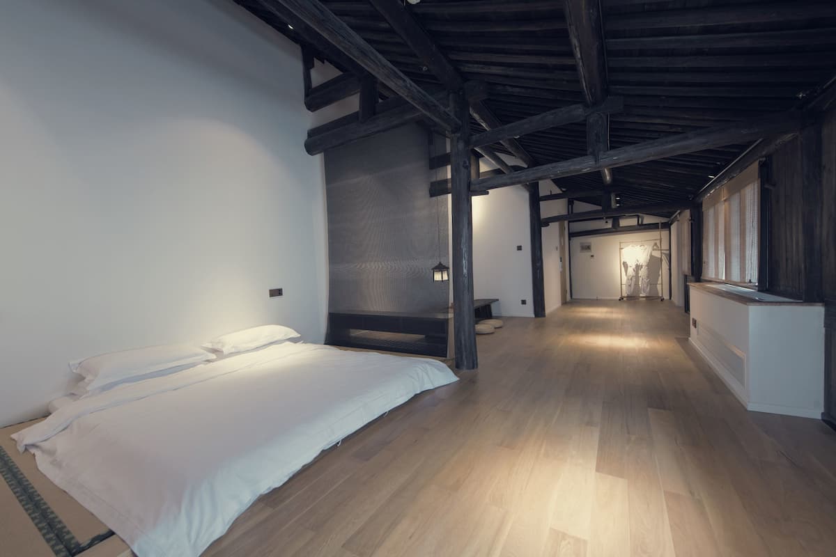 Una habitación amplia con una cama grande, suelo de madera y un techo alto con vigas a la vista.
