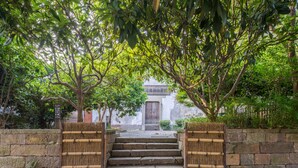A stone staircase leading to a traditional building with a wooden door, surrounded by lush greenery and stone walls. - Hangzhou Utea Guesthouse (Hangzhou)