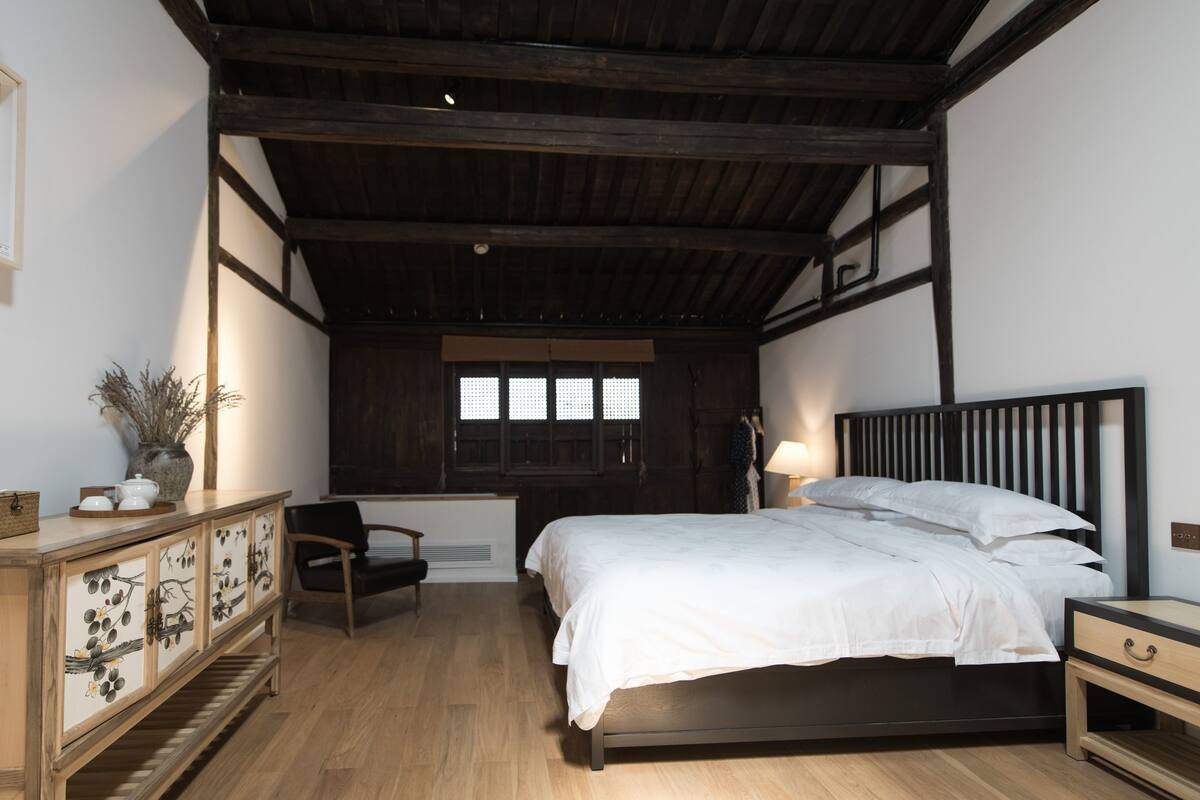Un dormitorio con una cama de madera, una mesita de noche, una silla, un armario con paneles decorativos y una ventana con persianas.