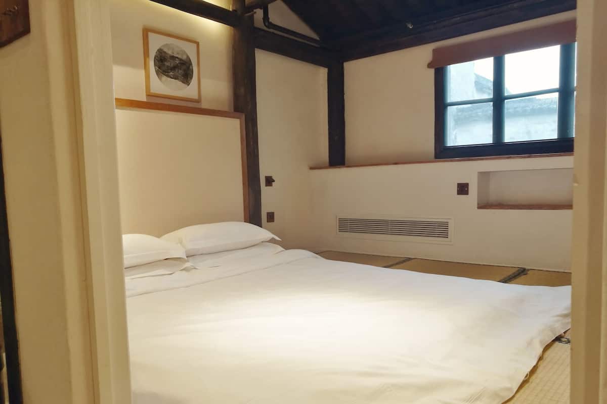 Un dormitorio con cama, ventana, un cuadro colgado en la pared y estantería empotrada.