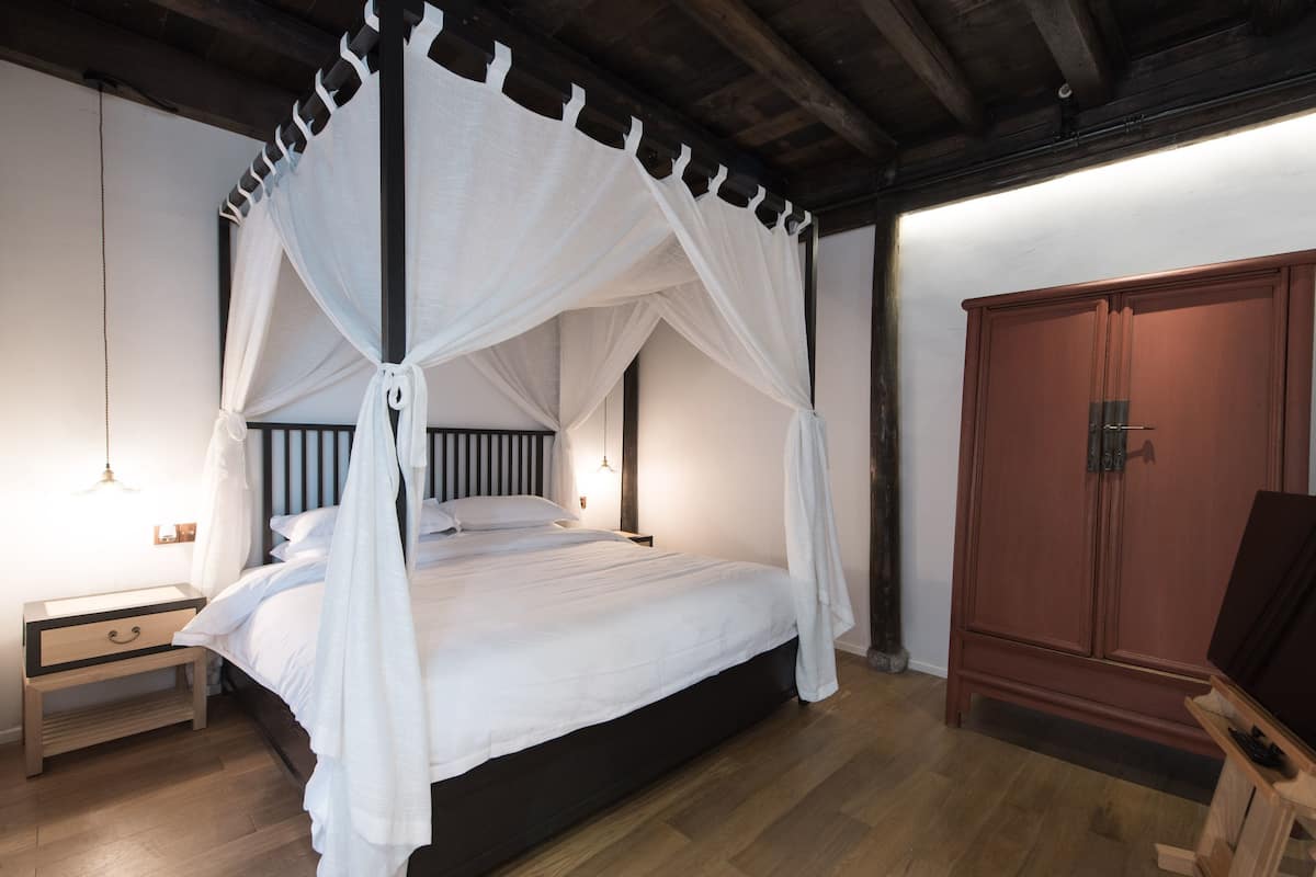 Un dormitorio con cama con dosel, suelo de madera y armario.