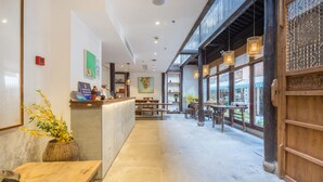 A spacious interior with a reception desk, wooden tables, and chairs, and large windows allowing natural light. - Hangzhou Utea Guesthouse (Hangzhou)