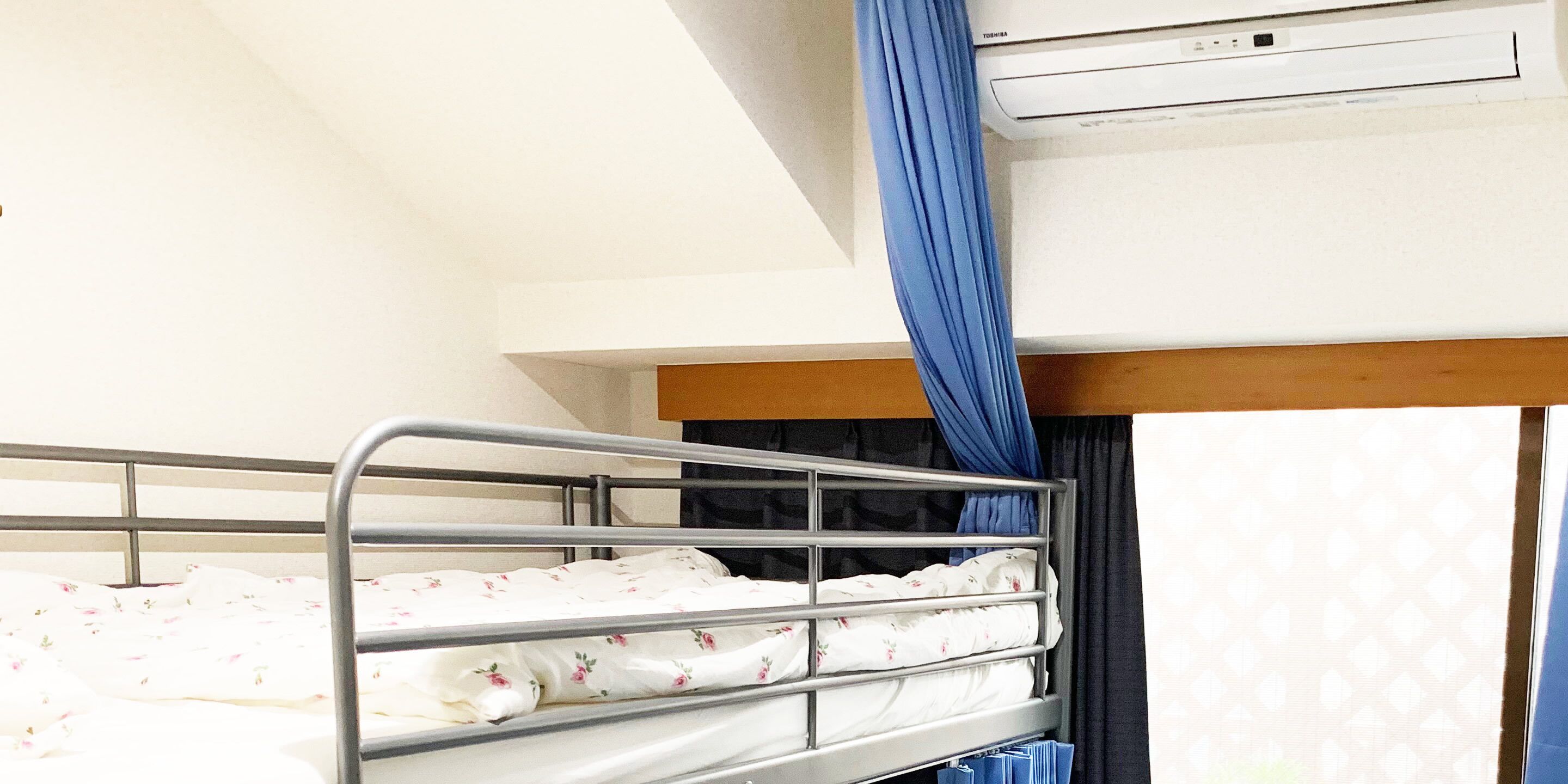 A bunk bed with a white mattress and floral bedding, a wooden headboard, and a window with blue curtains.