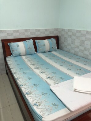 A single bed with a floral-patterned bedspread and two pillows, a wooden headboard, and a tiled wall. - Gold Hotel (Ho Chi Minh City)
