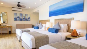 Habitación de hotel con dos camas, un escritorio y un ventanal con vistas al mar.