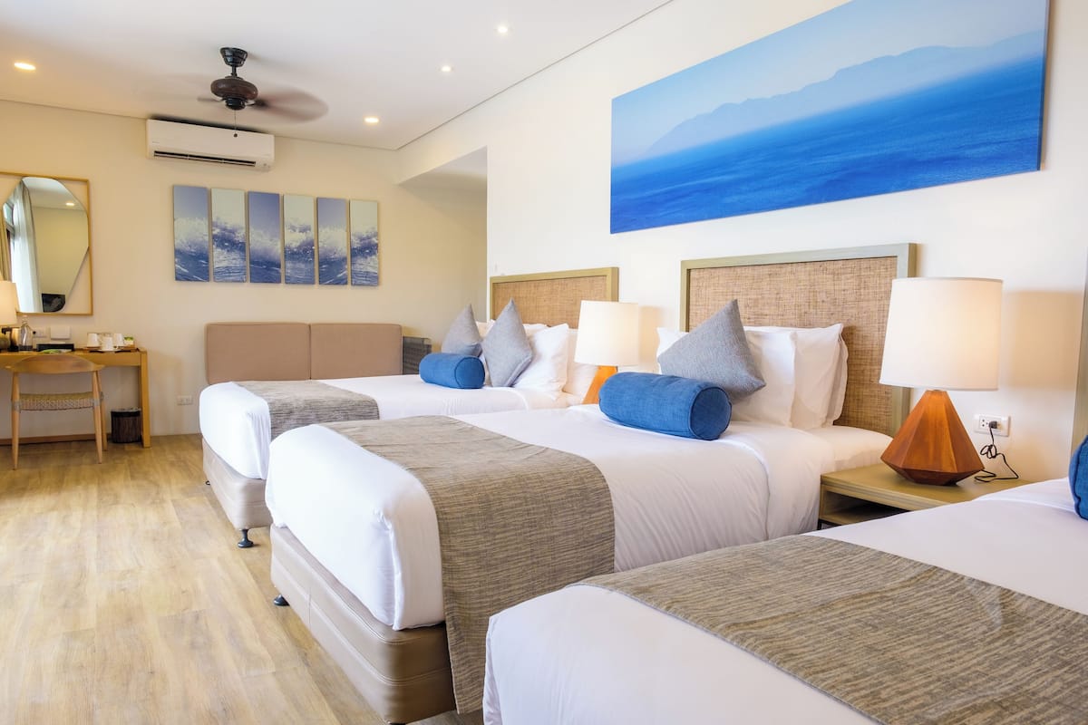A hotel room with two beds, a desk, and a large window with a view of the sea.