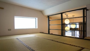Ein Raum mit Tatami-Matten, einer Schiebetür, einem großen Fenster und einer hängenden Leuchte.
