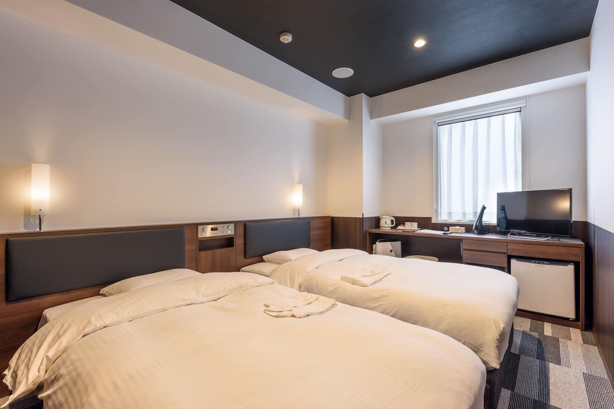 A hotel room with two beds, a desk, a television, and a small refrigerator.