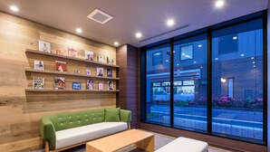 A modern room with a green sofa, a wooden table, and a large window with a view of a building and street. - Belken Hotel Kanda (Tokyo)