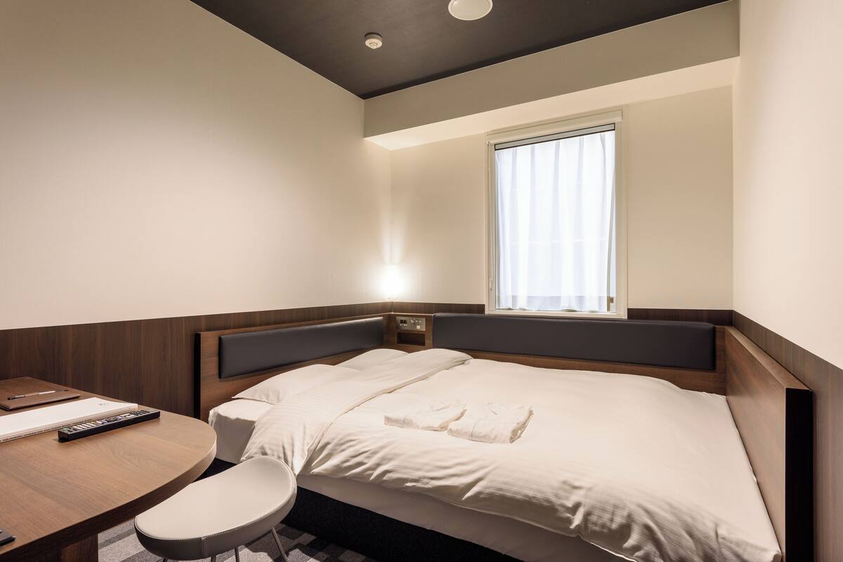 A modern hotel room with a bed, bedside table, and a small desk with a chair.