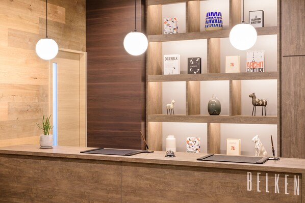 A reception desk with a wooden finish, two pendant lights, a potted plant, and a shelf with various decorative items and framed certificates.