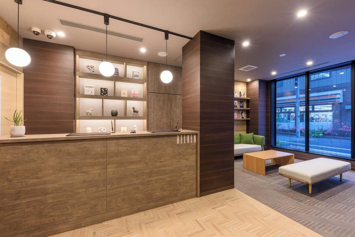 A modern reception area with a wooden reception desk, shelves with framed pictures, and a seating area with a sofa and ottoman.